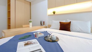 Ett hotellrum med en säng, ett sängbord, en liten avlastningsyta, en bokhylla och en vägghylla med en växt.