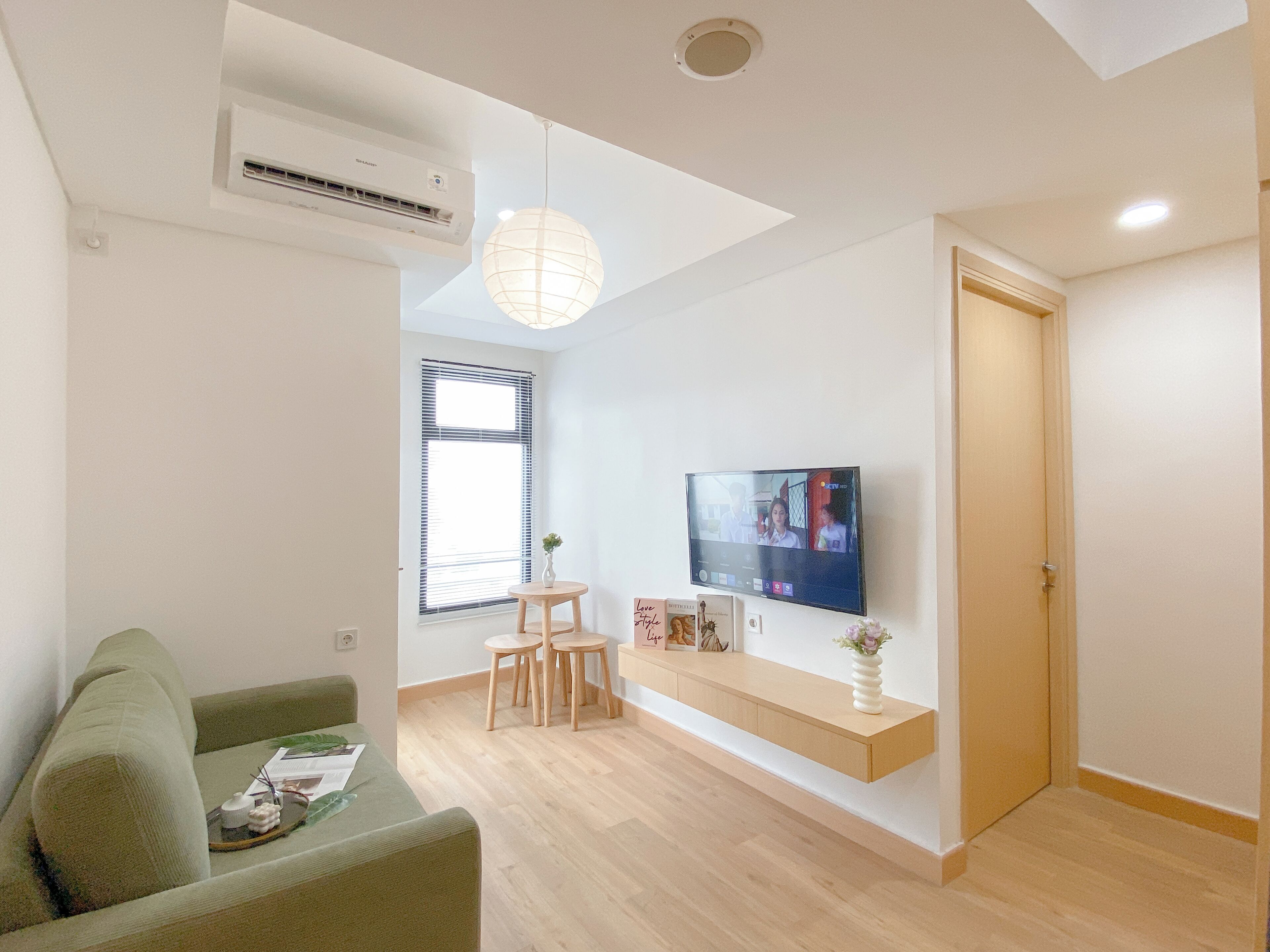 A modern living room with a green sofa, a wooden coffee table, a TV mounted on the wall, and a wooden door.