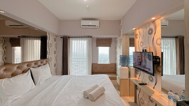 A hotel room with a large bed, a TV, a desk with a water dispenser, and a view of the city.