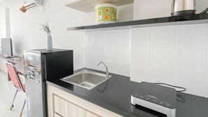 A modern kitchen with a black countertop, stainless steel sink, and a coffee maker on a shelf. - Basic Studio Room At Azalea Suites Apartment (Cikarang)