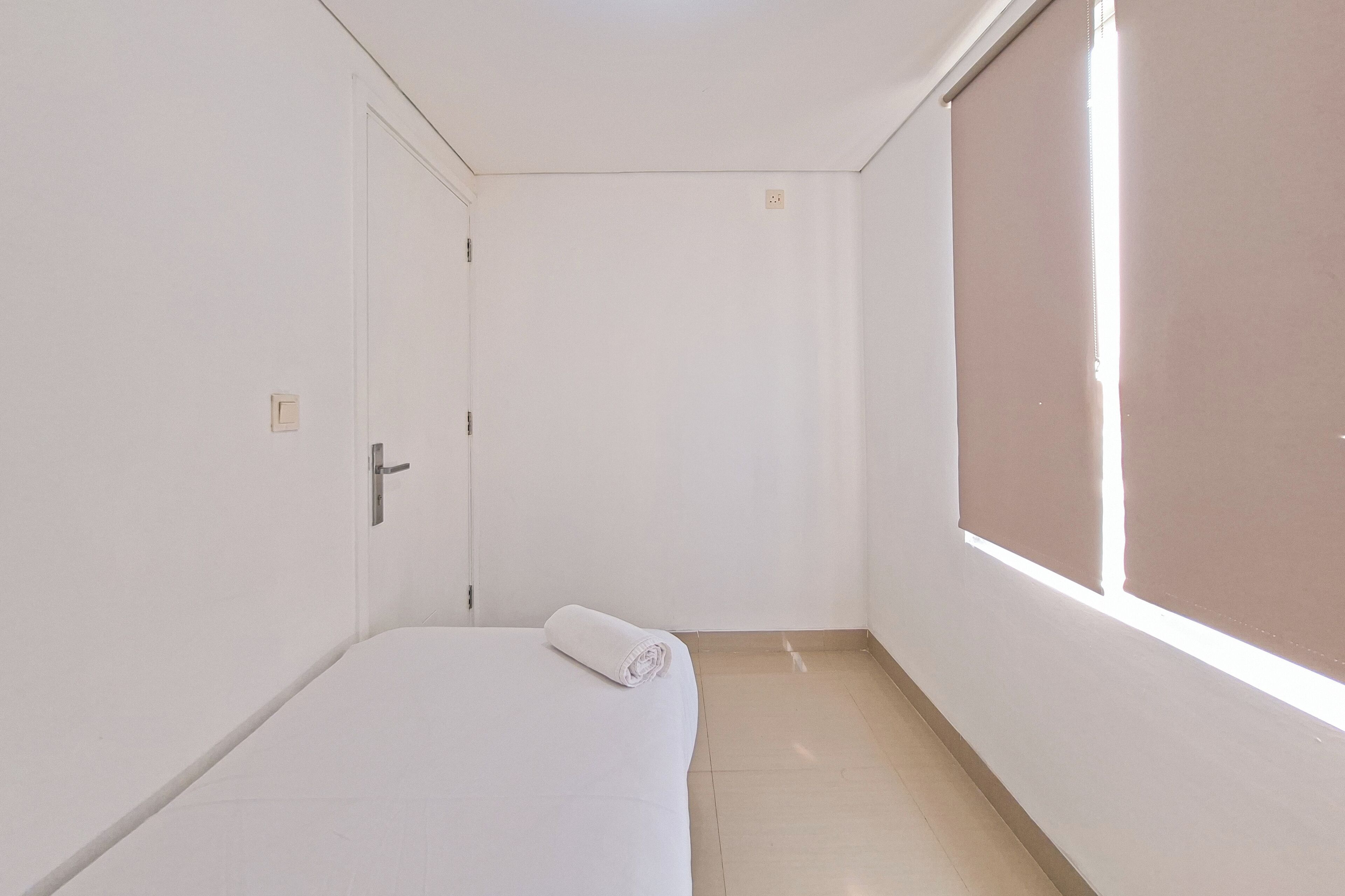 A small, white, single-bed room with a closed door and a window with blinds.