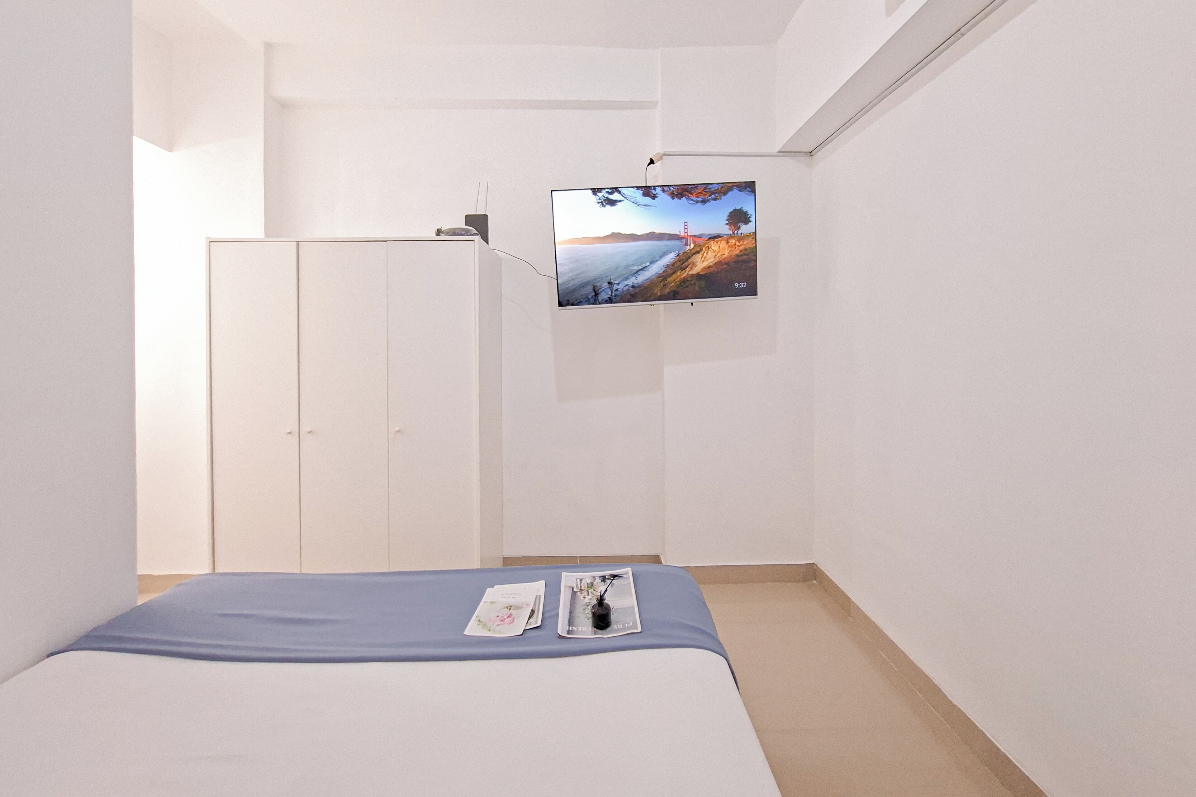 A bedroom with a bed, a TV mounted on the wall, a wardrobe, and a small table with items on it.