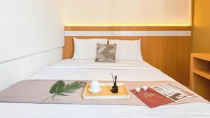 A neatly made bed with a wooden headboard, a tray with a small vase and incense sticks, a magazine, and a green leaf on the bed. - Spacious 2Br At Meikarta Apartment (Cikarang)