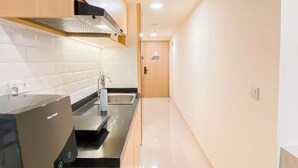 A modern kitchen with white tiles, a stainless steel range hood, and a black countertop. - Spacious 2Br At Meikarta Apartment (Cikarang)