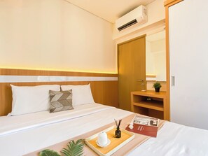 Una habitación de hotel con cama, mesita de noche, un espejo, un armario y un equipo de aire acondicionado.