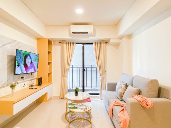 Una sala de estar moderna con un televisor de pantalla plana, un sofá, una mesita redonda y un balcón con cortinas.