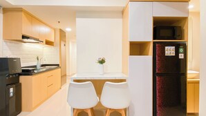A modern kitchen with wooden cabinets, a black refrigerator, and two white chairs. - Spacious 2Br At Meikarta Apartment (Cikarang)