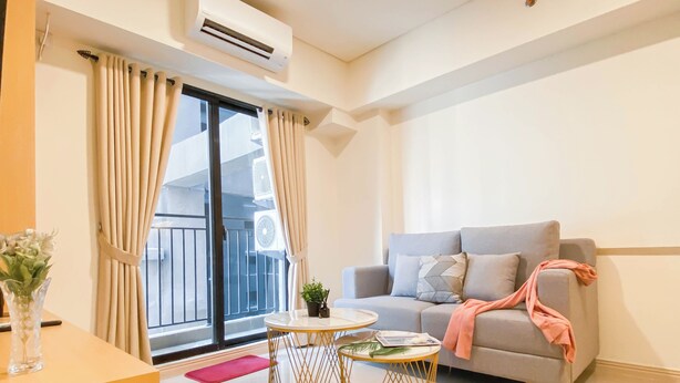 A modern living room with a grey sofa, a round gold-framed table, and a balcony with curtains. - Spacious 2Br At Meikarta Apartment (Cikarang)