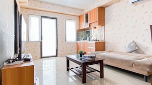 Una sala de estar con sofá, mesa de centro, televisor y una zona de cocina con armarios y ventana.