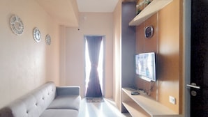 A living room with a sofa, a TV mounted on a wooden wall, and decorative plates on the wall. - 1Br Apartment At Tamansari Prospero Sidoarjo Near Lippo Mall Sidoarjo (Sidoarjo)