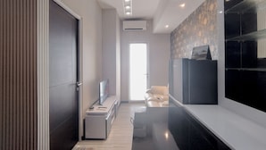 A modern hotel room with a sleek black and white color scheme, a flat-screen TV, a desk with a chair, and a large mirror. - Monochromatic Modern 1Br At Tamansari Prospero Sidoarjo Apartment (Sidoarjo)