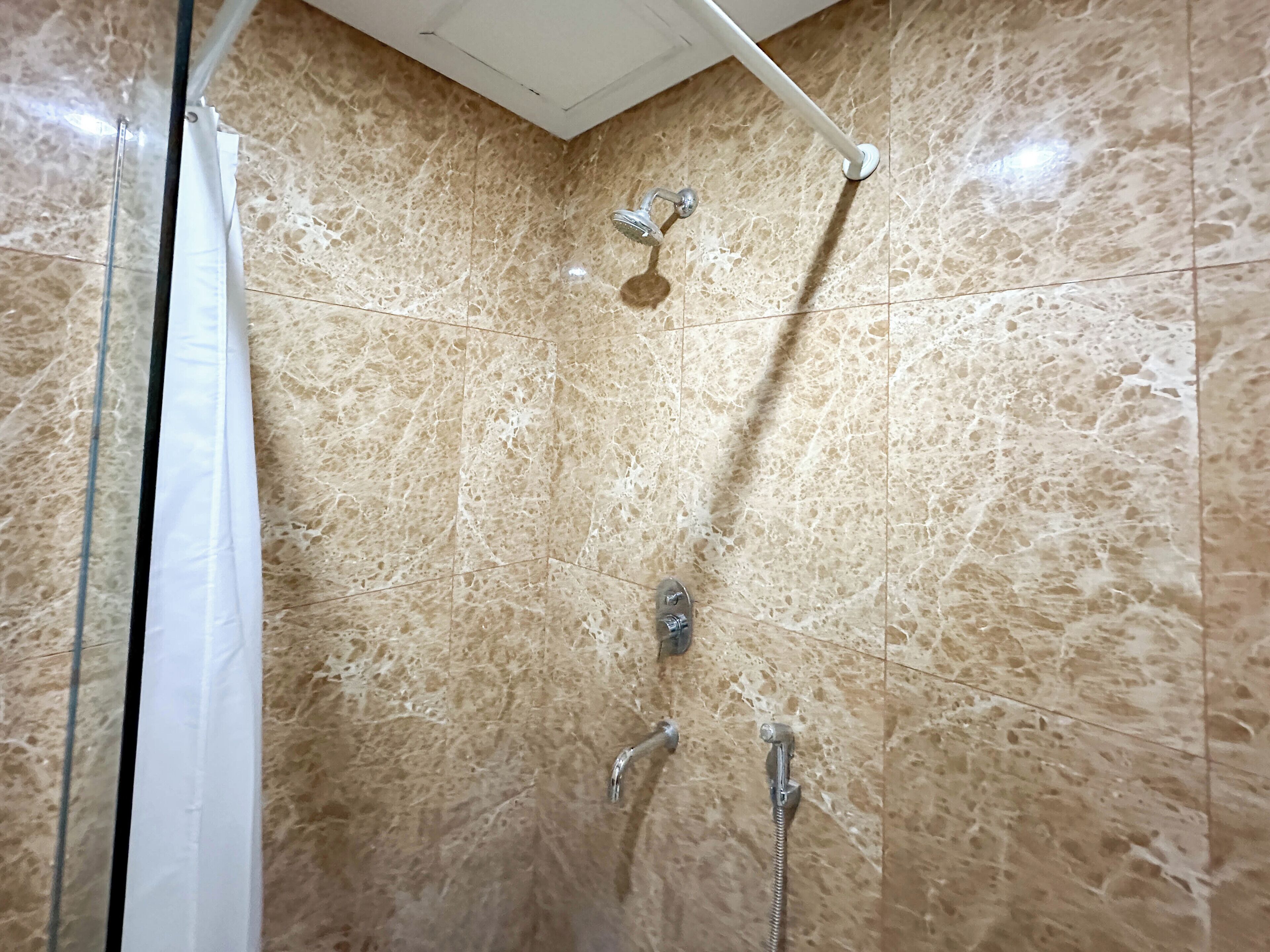 Une douche équipée d’un pommeau de douche à main et de deux robinets fixés au mur.