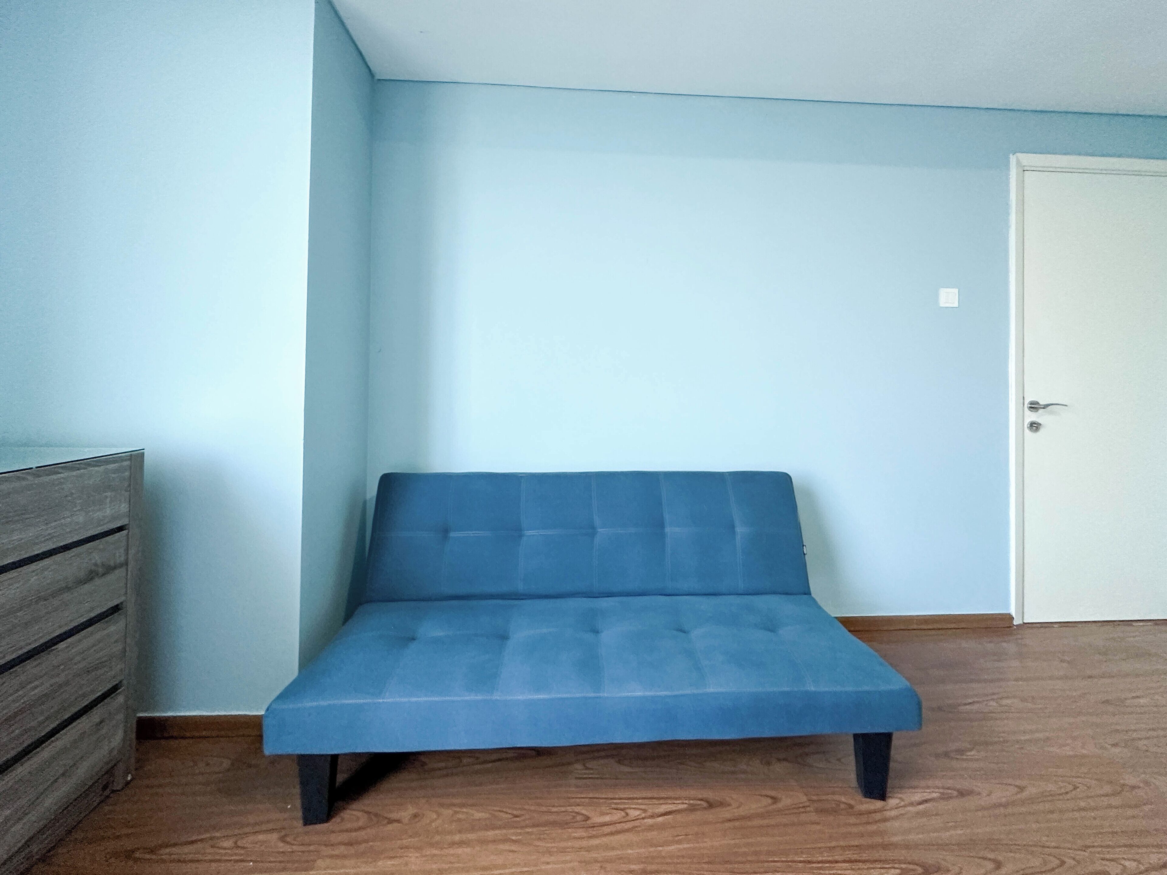 A room with a blue sofa, a wooden dresser, and a white door.