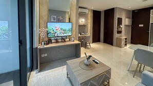Ein modernes Wohnzimmer mit Fernseher, einem kleinen Tisch mit Fernbedienung und einem Arbeitsbereich.