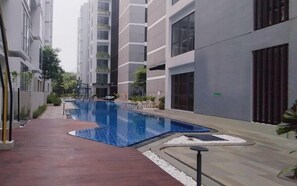 A modern residential building with a swimming pool, a red pathway, and a small garden area. - Tranquil And Modern Haven 2Br At The Rosebay Apartment (Surabaya)