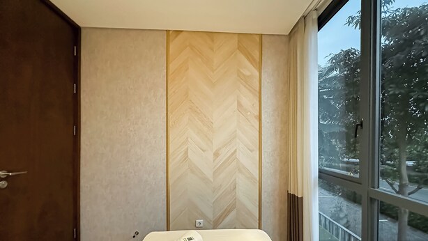 Una habitación de hotel moderna con un ventanal grande, suelo de madera y una cama con una toalla enrollada y un control remoto.
