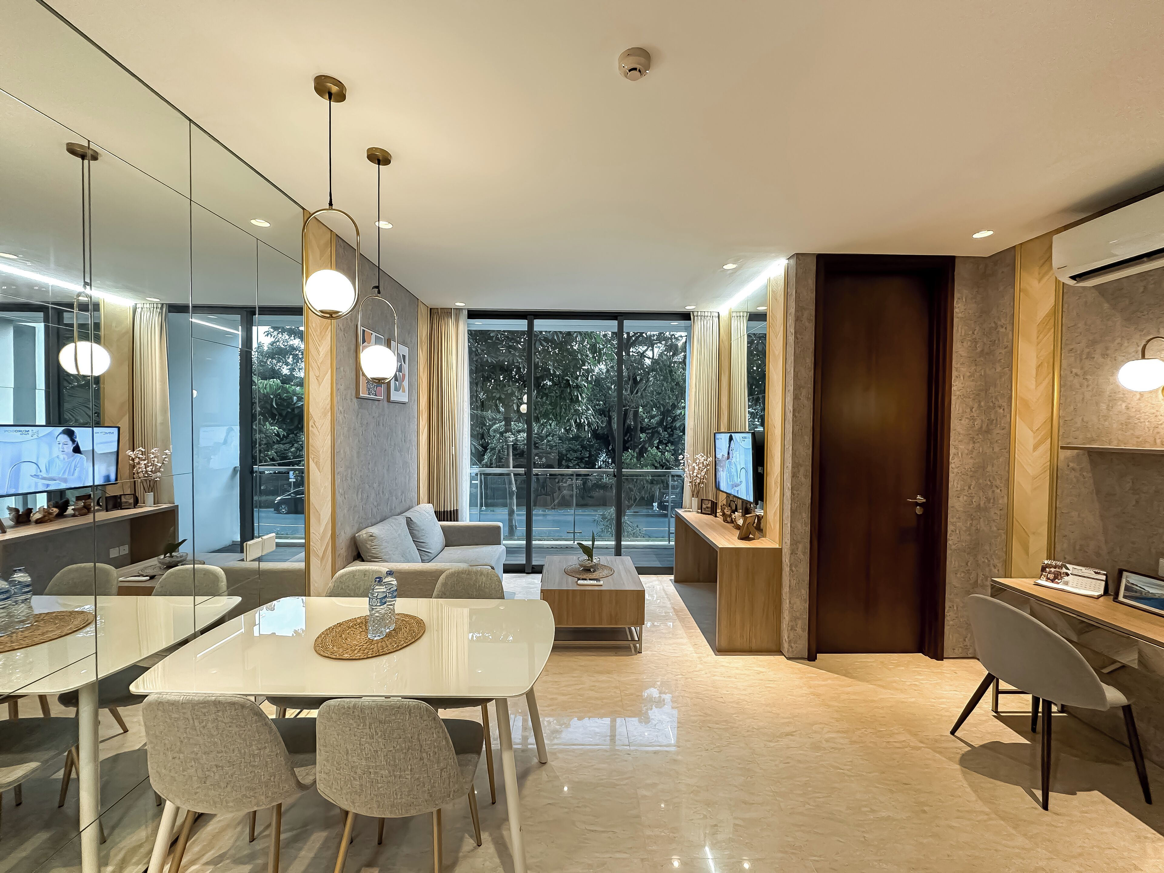 A modern hotel room with a dining area, a sofa, a TV, and a large window offering a view of the outdoors.