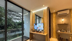 Una habitación de hotel moderna con un ventanal grande, un televisor de pantalla plana, un escritorio de madera, una silla y una mesita con un control remoto.