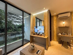 Ein modernes Hotelzimmer mit großem Fenster, einem Flachbildfernseher, einem Holztisch, einem Sessel und einem kleinen Tisch mit Fernbedienung.