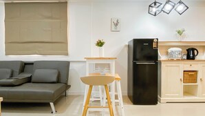 A modern living room with a grey sofa, a white table, and a black refrigerator. - Neat Style 2Br Apartment Meikarta (Cikarang)