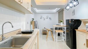 A modern kitchen with a built-in sink, a black refrigerator, wooden stools, and a dining table. - Neat Style 2Br Apartment Meikarta (Cikarang)