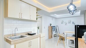 A modern kitchen with white cabinets, a sink, and a dining area with a table and chairs. - Neat Style 2Br Apartment Meikarta (Cikarang)