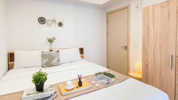 A neatly arranged hotel room with a bed, bedside table, and a bedside lamp. - Neat Style 2Br Apartment Meikarta (Cikarang)