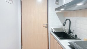 Een kleine keuken met een houten deur, een witte tegelachtergrond en een zwarte kraan.