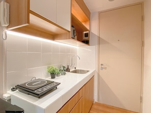 A modern kitchen with white tiles, a built-in oven, and wooden cabinets. - Neat And Warm Studio At Tokyo Riverside Pik 2 Apartment (Teluknaga)