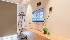 Ett modernt rum med ett bord i trä, en väggmonterad TV som visar en meny, en liten krukväxt och en hylla i metall.