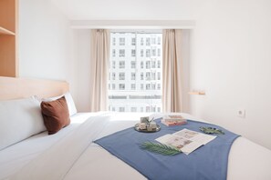 Una camera d'albergo con un letto, una finestra con tende, vista su un edificio e un vassoio con oggetti sul letto.