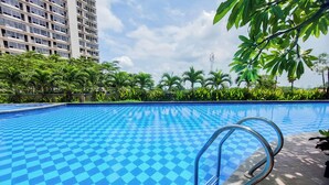 A swimming pool with a checkered pattern, surrounded by greenery and a tall building in the background. - Pleasant Studio Apartment Parkland Avenue (South Tangerang)
