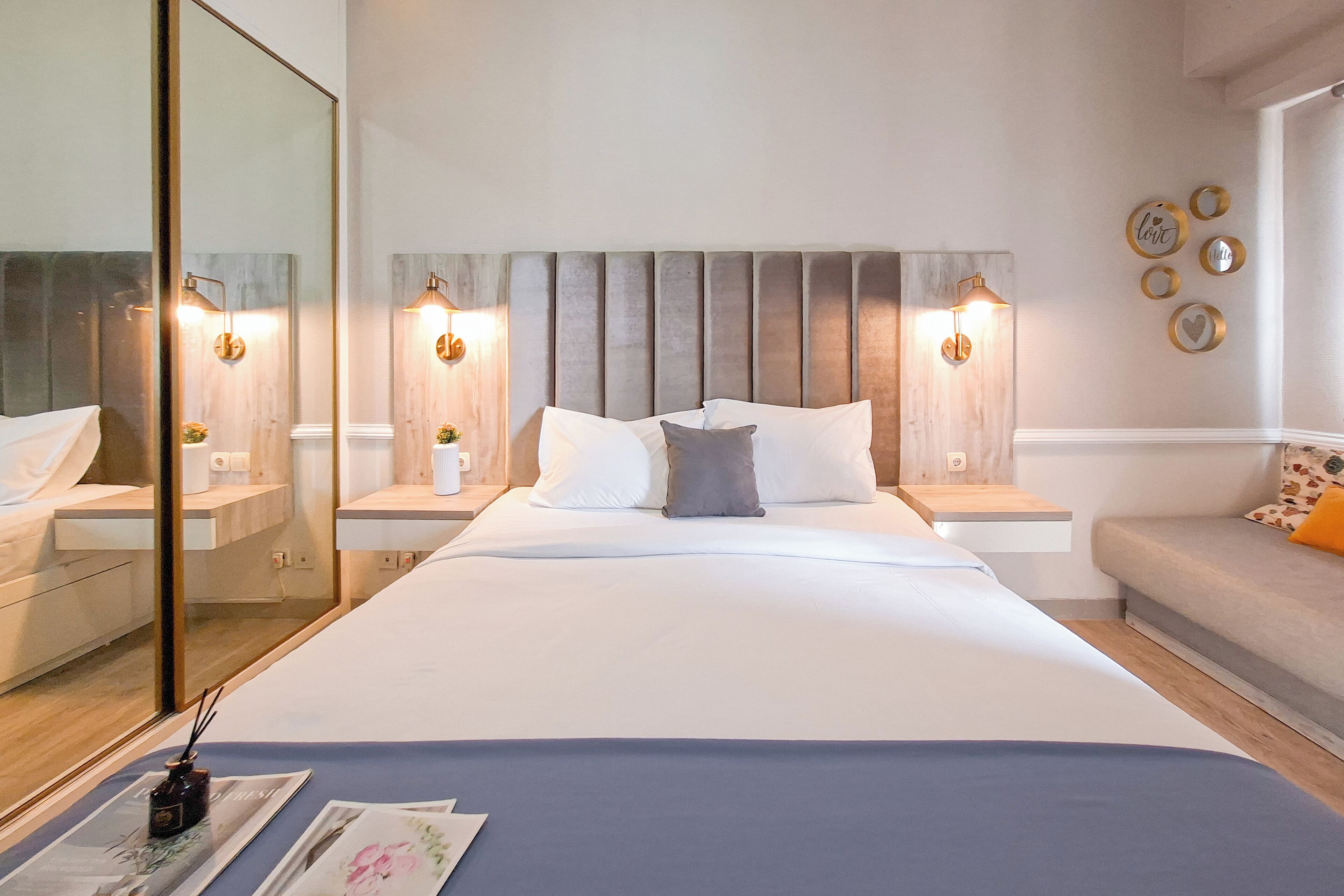 Ett modernt hotellrum med en stor säng, sängbord, en spegel och dekorativa vägglampor.