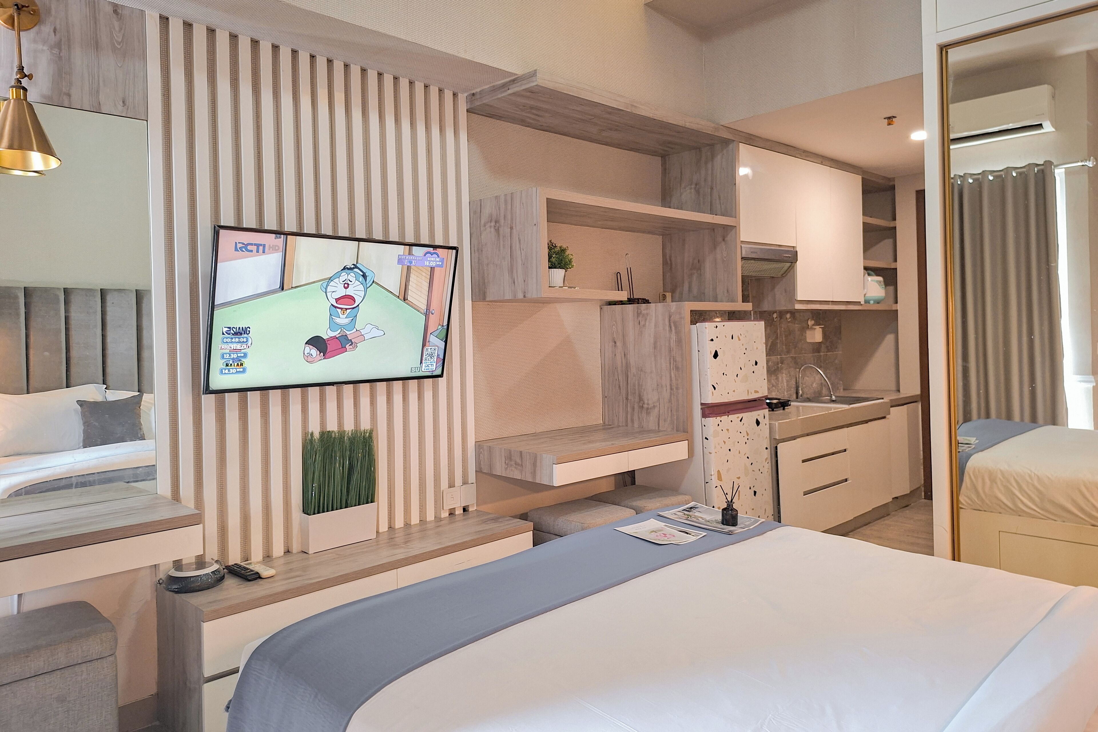 Habitación de hotel moderna con una cama grande, un televisor montado en la pared, una kitchenette y un baño con cortina de ducha.