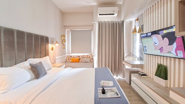 A modern hotel room with a large bed, a bedside table, a TV mounted on the wall, and a small seating area with a table and chairs. - Pleasant Studio Apartment Parkland Avenue (South Tangerang)