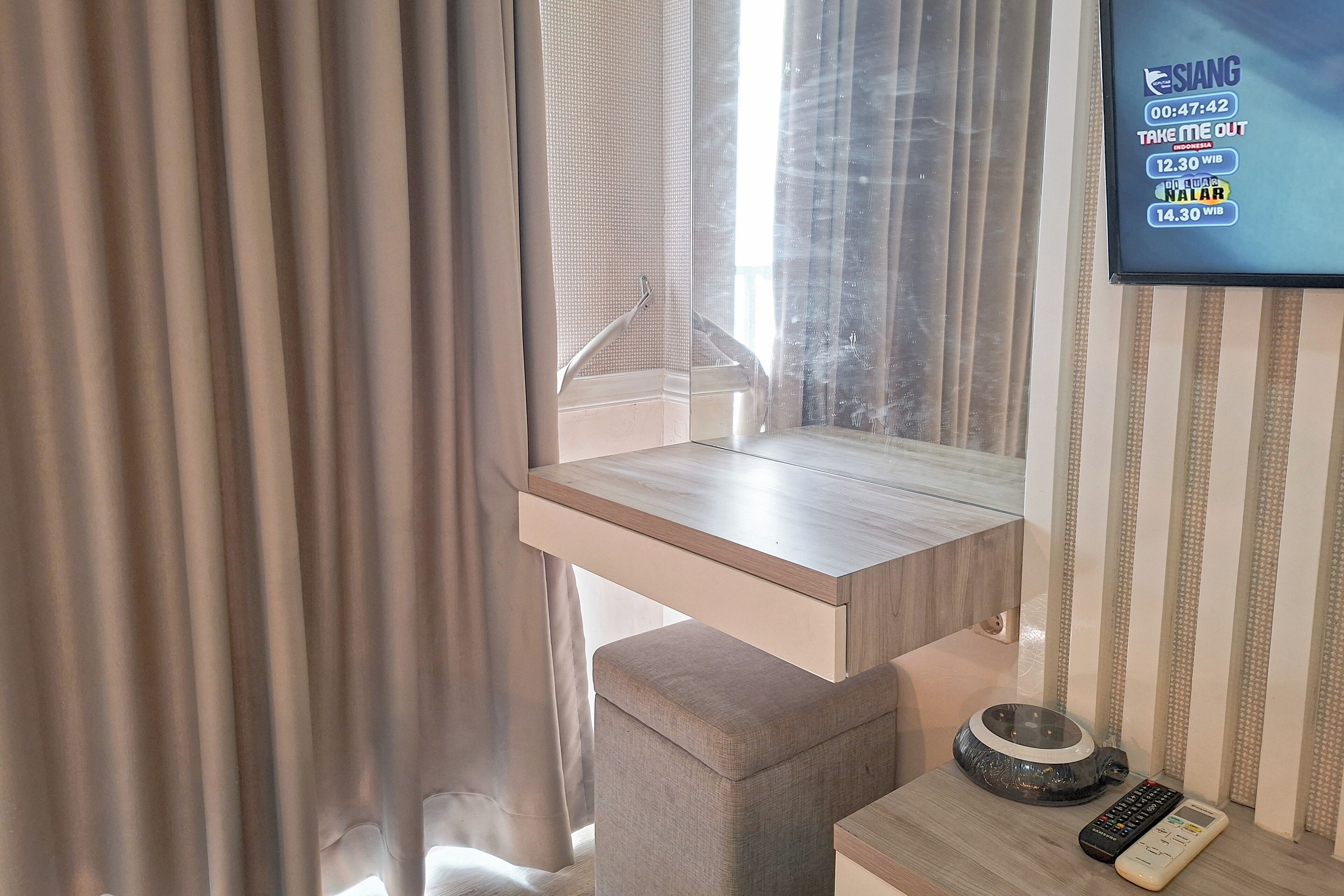 Camera d'albergo con un comodino in legno, un telecomando e una televisione a muro che mostra un palinsesto.