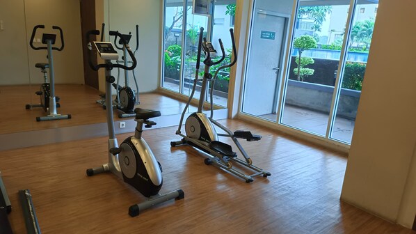 An indoor gym with exercise equipment, large windows, and a wooden floor.
