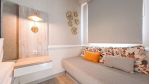 A modern bedroom with a wooden headboard, a bedside table, a sofa with floral cushions, and wall-mounted light fixtures. - Pleasant Studio Apartment Parkland Avenue (South Tangerang)