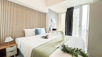 Quarto de hotel moderno com uma cama grande, mesa de cabeceira, cortinas e vista para a cidade.
