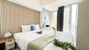 A modern hotel room with a large bed, a bedside table with a lamp, a small desk, and a view of the city through the window. - Nice Studio Near Tokyo Hub At Tokyo Riverside Pik 2 Apartment (Teluknaga)