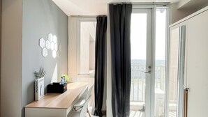A modern room with a wooden desk, a view of the city through large windows, and a balcony with a railing. - Nice Studio Near Tokyo Hub At Tokyo Riverside Pik 2 Apartment (Teluknaga)