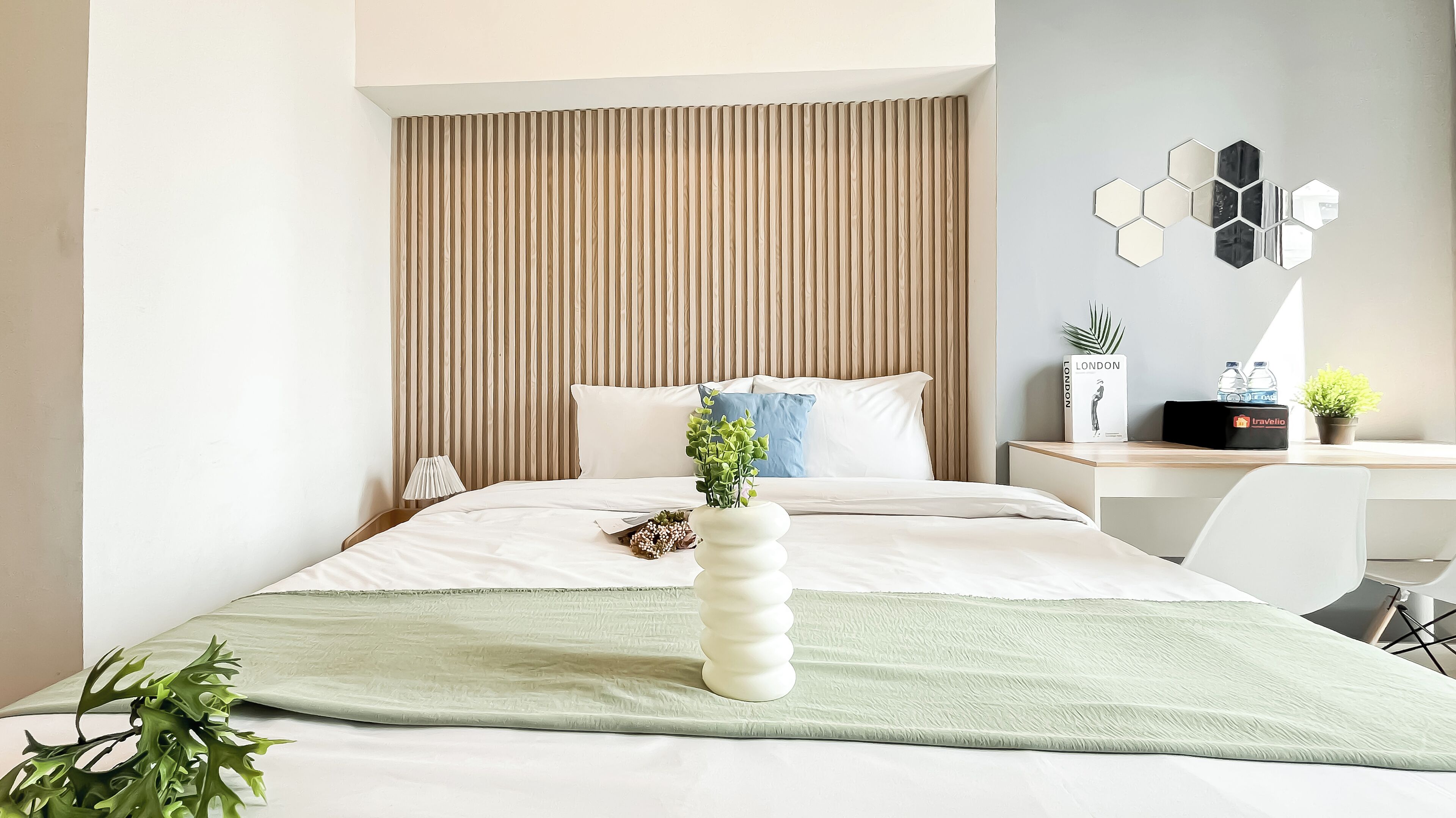 Une chambre d’hôtel moderne équipée d’un lit, d’un bureau, d’une plante en pot et d’un élément décoratif mural.
