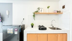 A kitchen with a refrigerator, a gas stove, a sink, and a shelf with decorative items. - Nice Studio Near Tokyo Hub At Tokyo Riverside Pik 2 Apartment (Teluknaga)