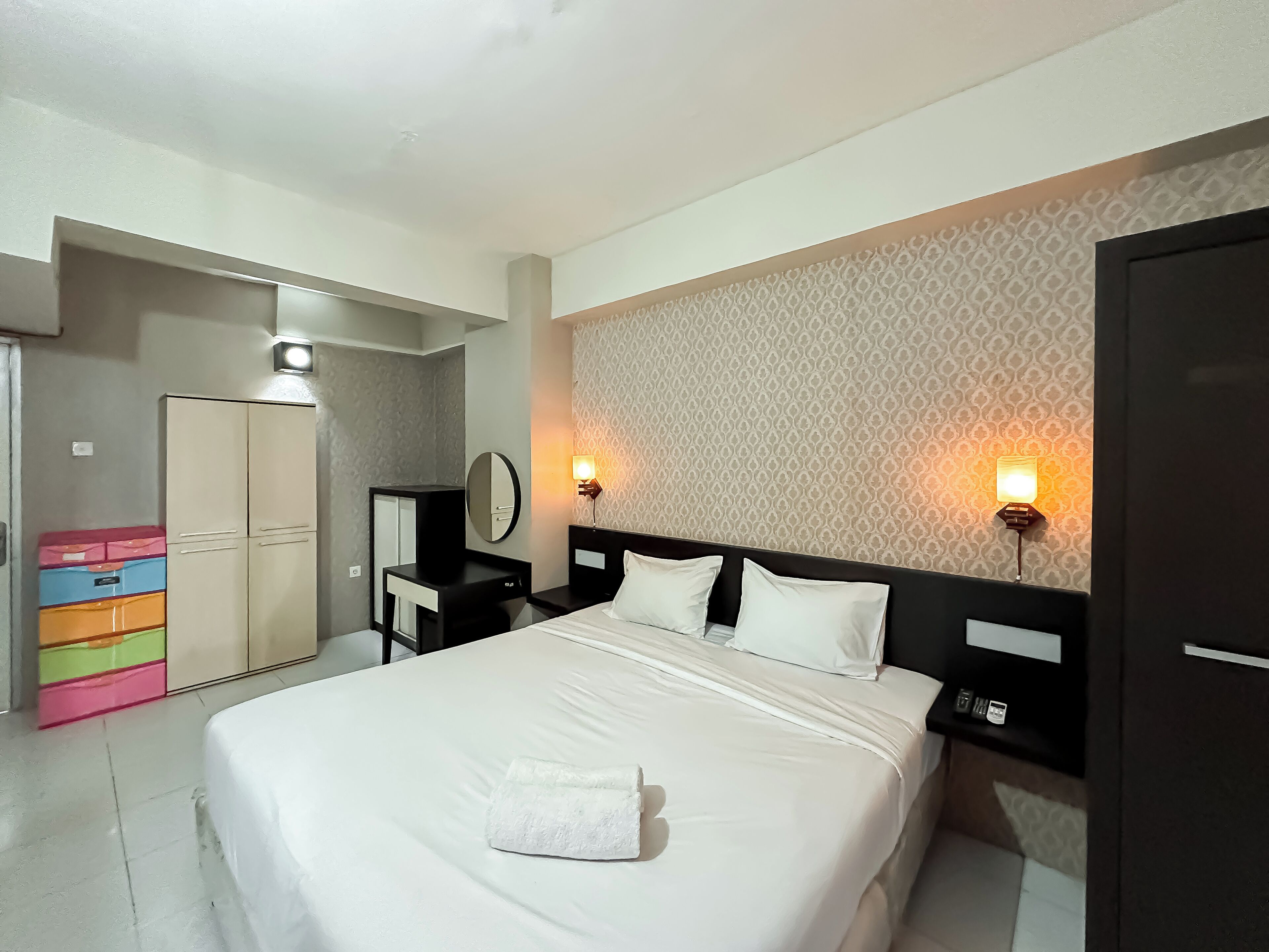 A hotel room with a bed, bedside tables, a wardrobe, and patterned wallpaper.