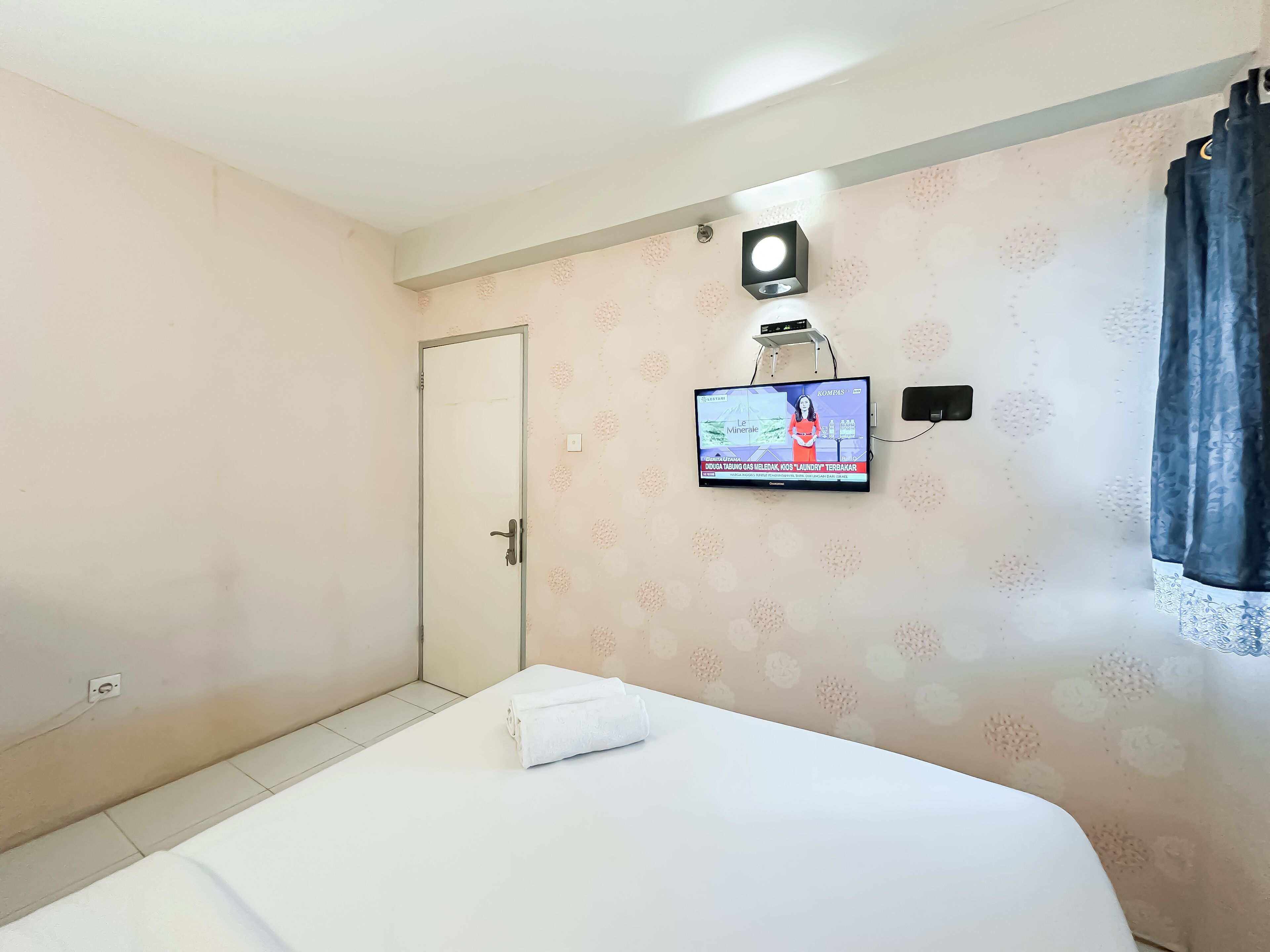 Ein Hotelzimmer mit einem Bett, einem an der Wand montierten Fernseher und einer Tür.