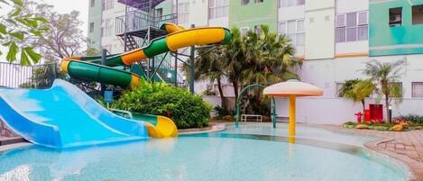 A swimming pool with a water slide and a sun shelter.