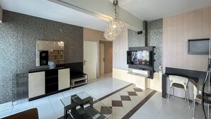 A modern living room with a TV, a fireplace, a dining area, and a patterned wall. - 3Br Combined Spacious At Dian Regency Apartment (Surabaya)