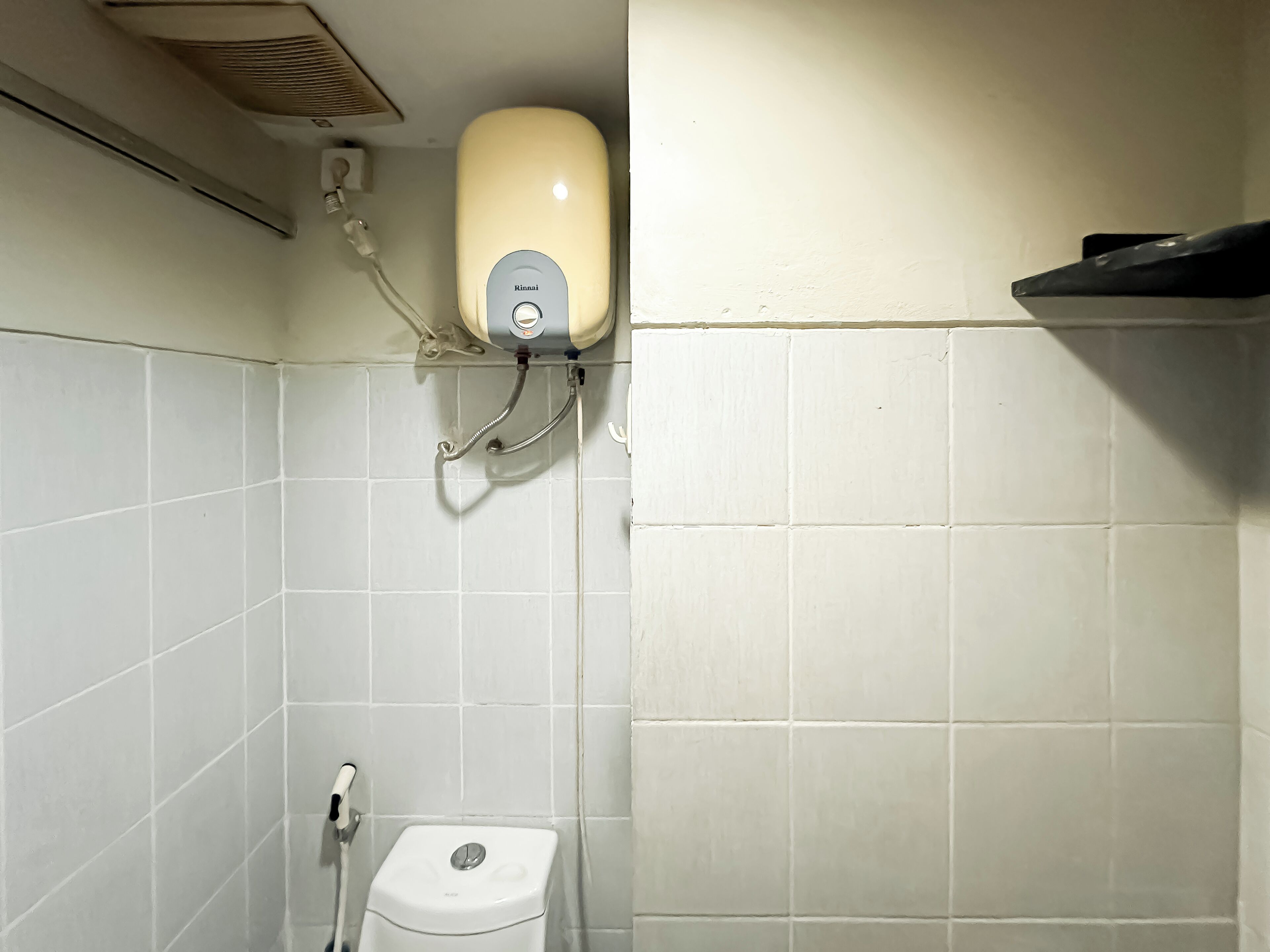 Un baño con paredes de azulejos blancos, un inodoro y un secador de manos instalado en la pared.