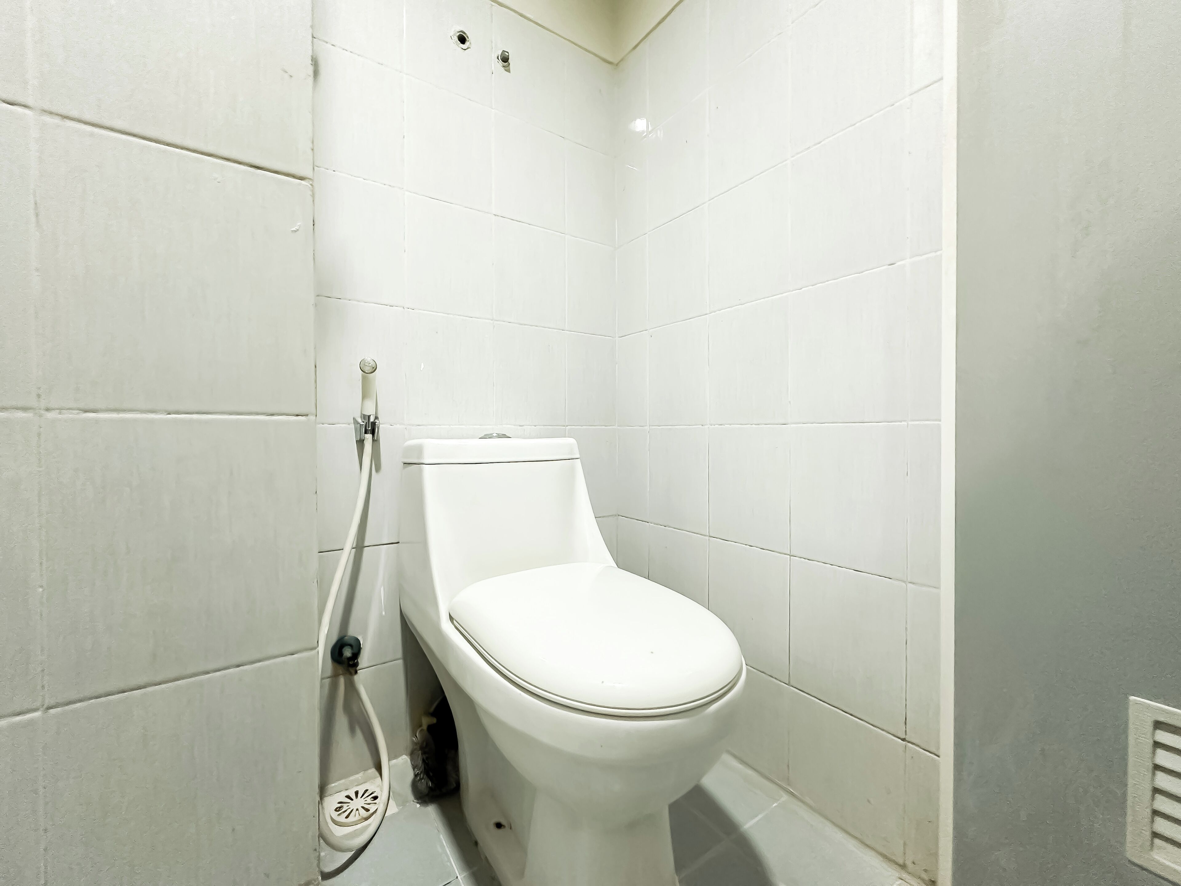 A white toilet in a bathroom with white tiles on the walls.