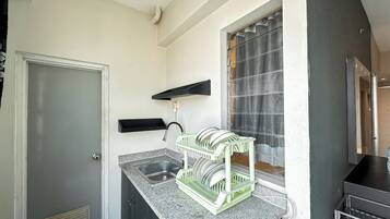 A kitchen with a granite countertop, a dish rack, a black shelf, and a window with curtains.